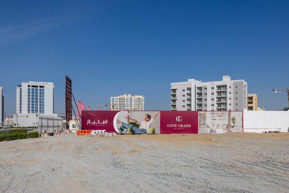 Cove Grand By Imtiaz A construction site featuring a large advertisement for "Cove Grand" amid urban buildings and clear blue skies.